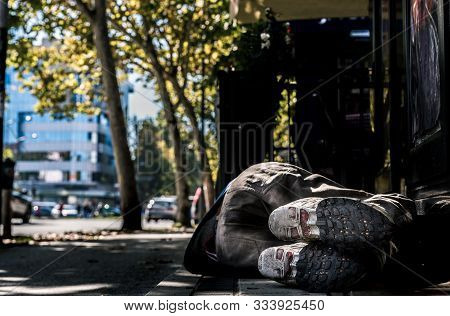 Homeless Man, Poor Homeless Man Or Refugee Sleeping On The Concrete Sidewalk Floor Ground On The Urb