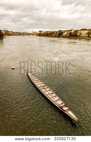 Long Rowing Boat In The Rhine River In Switzerland With Old City Center Of Basel With Munster Cathed