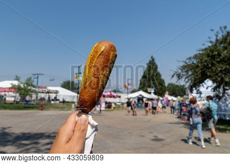 Hand Holds Up A Pronto Pup Smothered In Mustard At The Fairgrounds In Summer