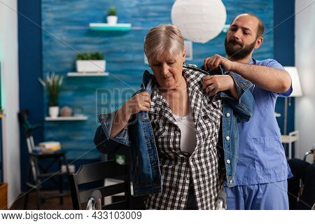 Social Asisstant Man Worker Helping Pensioner Disabled Senior Woman Puts Jacket During Recovery Sess