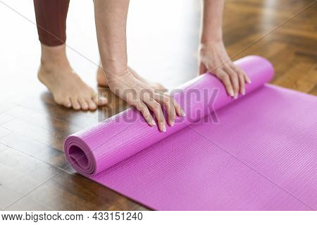 Young Woman Rolling Her Yoga Mat After Exercising And Doing Meditation At Home