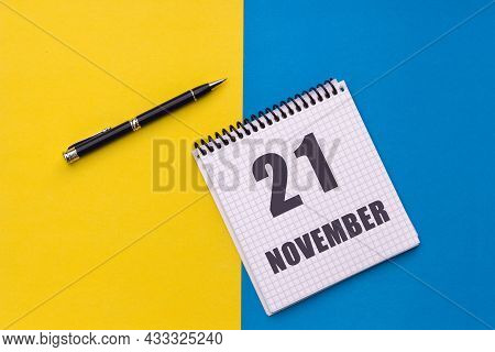 November 21th. Day 21 Of Month. Calendar Date. Notebook With A Spiral And Pen Lies On A Yellow-blue 