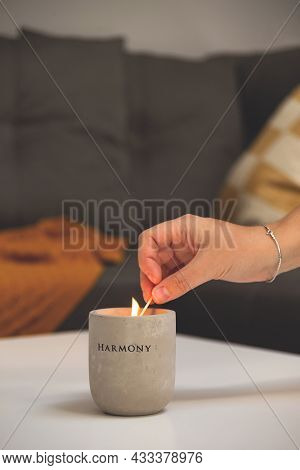 Woman Lights Candle In Concrete Candlestick On Table In Living Room Next To Sofa With Pillows And Bl