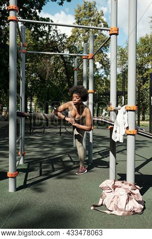 Young active woman in tracksuit exercising by sports facilities in the morning