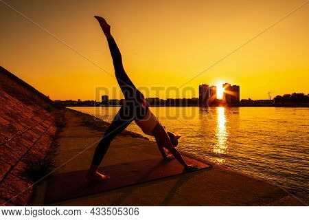Young Woman Is Exercising Outdoor. She Is Practicing Yoga On Sunny Day. Eka Pada Adho Mukha Svanasan