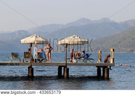 Hisaronu, Turkey​ -​ September 2021: People Sunbathing On A Beach On Green Mountains Background. Tou