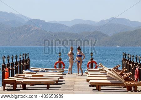 Hisaronu, Turkey​ -​ September 2021: Two Happy Girls In Bikini Sunbathing On A Beach On Green Mounta