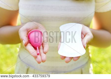 Young Woman Showing Menstrual Cup And Sanitary Pad In Hands Against Green Natural Background. Femini