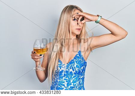 Young beautiful caucasian woman drinking a glass of white wine smelling something stinky and disgusting, intolerable smell, holding breath with fingers on nose. bad smell 