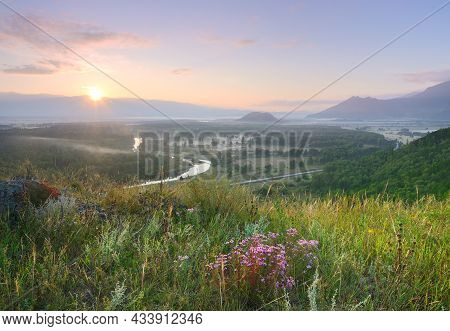 A Blooming Mountain Slope Above The Katun Valley, The Sun Above The Horizon Under A Golden-blue Sky 