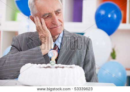 Sad senior man forgot how old is looking at birthday cake with a question mark