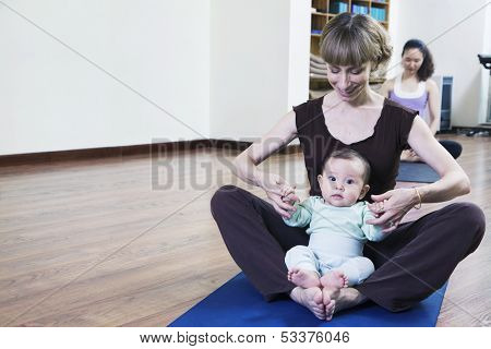 Mother and baby sitting cross-legged and doing yoga in yoga class