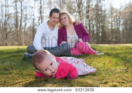 Baby Girl In The Grass Parents On The Background