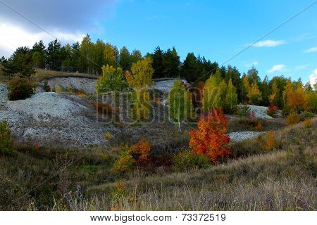 cascade of limestone hills covered with trees with autumn foliage on background of blue sky