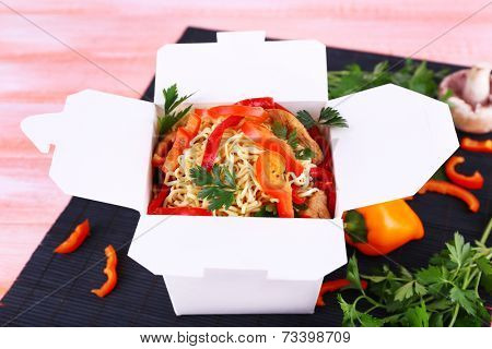 Chinese noodles in takeaway box on black mat on pink background