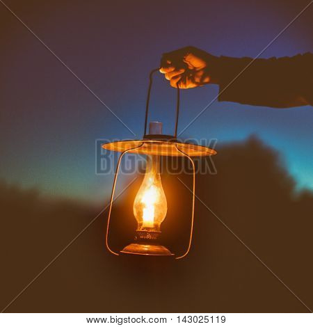 hand holds a large lamp outdoors in the dark. old lamp with a candle illuminates the the way on a dark night