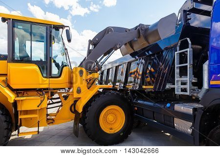 Image of a yellow backhoe using a scoop to load soil into truck, isolated on white background