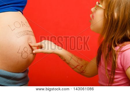 Closeup pregnant woman belly with loading concept painted on her tummy. little girl with amazed face expression pointing on belly her mom