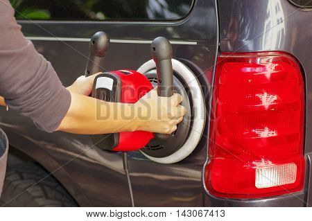 man with a power buffer machine cleaning the back part of a car.