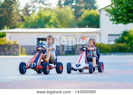 Two active little kid boys driving pedal race cars in summer outdoors. Children, best friends racing with fast speed and having fun. Twins making competition