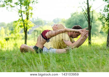 Young couple doing yoga at the park. Acroyoga.
