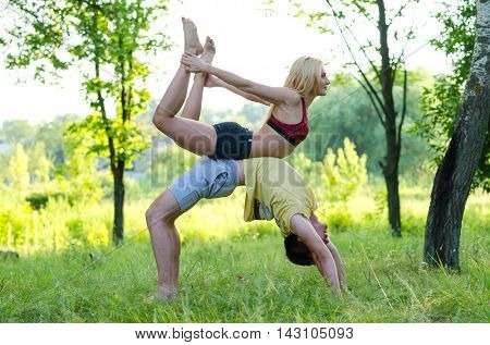 Young couple doing yoga at the park. Acroyoga.