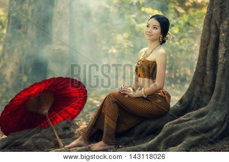 Thailand Girl in traditional costume sitting on tree roots.