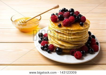 Homemade pancakes with honey and fresh berries. Stack of breakfast pancakes served with blueberry raspberry and blackcurrant.