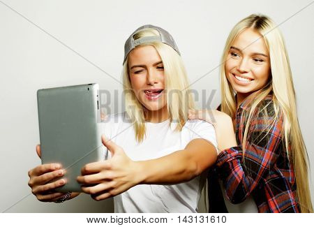 two hipster girls friends taking selfie with digital tablet, studio shot over gray vackground