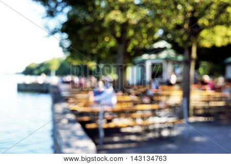 defocused bokeh background. people sitting in beergarden at lake.