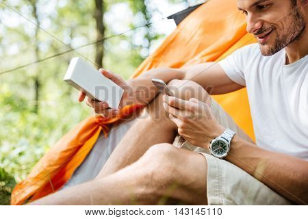 Smiling young man tourist using mobile phone and portable mini speaker in forest