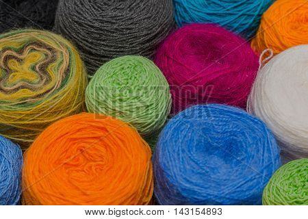 Many small balls of wool of rainbowcolors on the wooden table.
