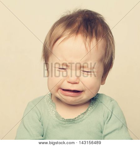 Little baby with darg hair crying on gray background