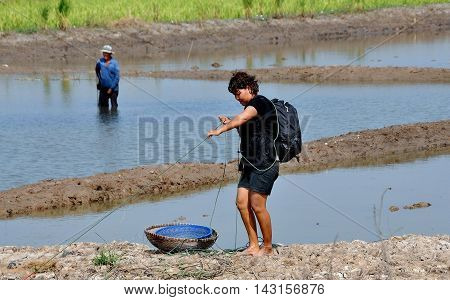 Ayutthaya Thailand - December 19 2010: Thai woman wearing a backpack fishing in flooded pools divided by earthen berms