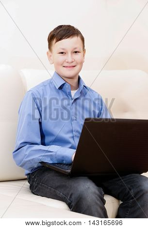 Boy sitting on sofa with black laptop.