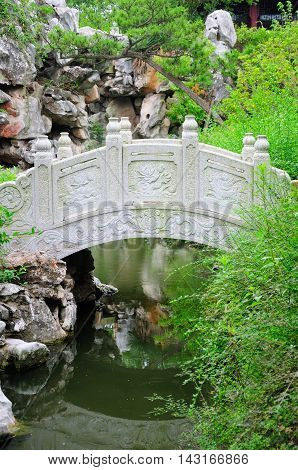 A curved bridge over a small stream within the classical Chinese li yuan garden in Zhaojialou in Shanghai china on an overcast day.