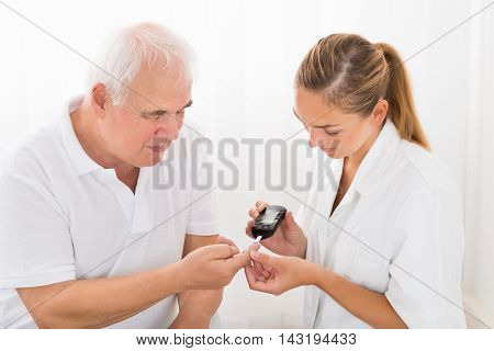 Young Female Doctor Using Glucometer On Senior Male Patient's Finger