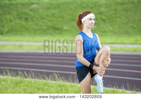 Young Red Haired Ginger Caucasian Female in Athletic Sportgear Having Legs Stretching Excercises Outdoors. Horizontal Image Orientation