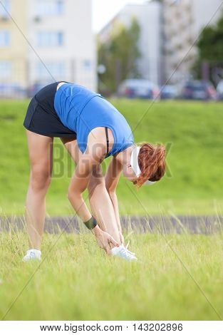 Young Red Haired Ginger Caucasian Female in Athletic Sportgear Having Arms Stretching Excercises Combined with Trunk Bending Outdoors.Vertical Image