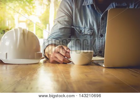 engineering useing laptop computer note someting with pen at notbook and holding a cup of coffee on wooden table. vintage effect.