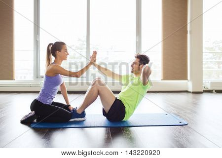 fitness, sport, training, teamwork and people concept - happy woman with personal trainer doing sit ups and high five gesture in gym