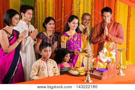 cheerful indian family celebrating or praying Lord Ganesh or ganpati bappa on ganesh festival or ganapati festival or ganesh utsav or ganeshotsav at home with puja thali