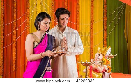 good looking Indian young couple performing puja in front of lord ganesh on ganesh festival or ganesh utsav or ganpati festival