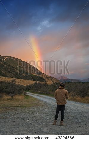 Man looking at rainbow over mountain near Lake Pearson / Moana Rua Wildlife Refuge located in Craigieburn Forest Park in Canterbury region South Island of New Zealand