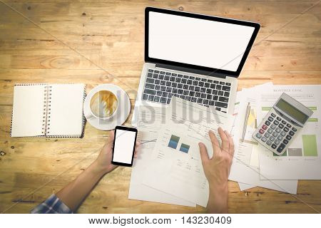 A man hand holding smart phone and discussing on stockmarket charts on wood desk in office with vintage effect.