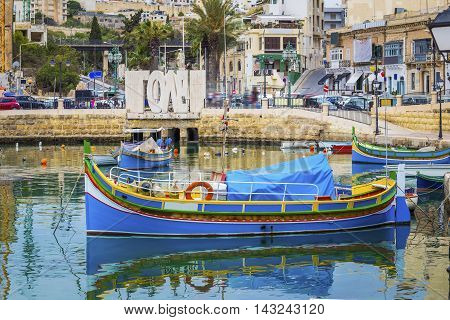 Malta, Spinola bay - Famous maltese Luzzu fishing boat with Love sign at background, St.Julians