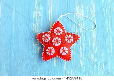 Red Christmas star ornament isolated on a blue wooden background. Handmade felt star with white circles. Christmas home decor. Winter kids crafts. Closeup. Top view