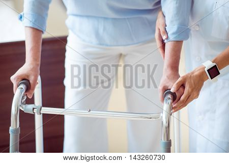 Medical service. Cropped image of professional doctor helping senior woman with walking frame