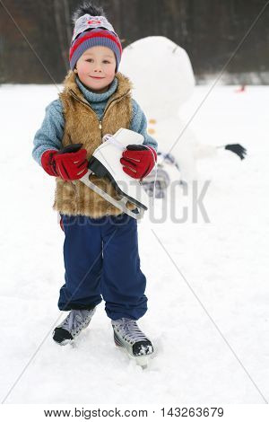 Little handsome boy with skate stands near upside down snowman at winter day