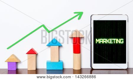 Marketing strategy growing concept on tablet. Toy block rise with Marketing success diagram graph. Tablet with hi tech tech text Marketing success rising up.
